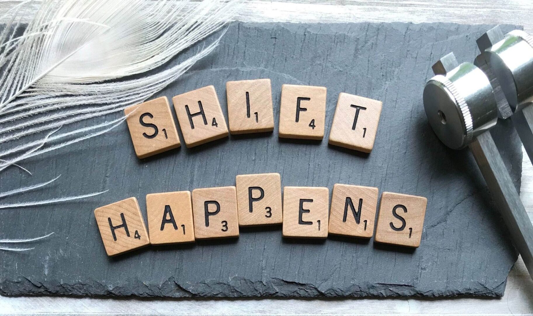 A slate with scrabble tiles that spell out " shift happens ".